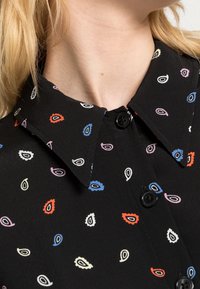 Czarna koszula z kołnierzykiem, ozdobiona wielokolorowym wzorem w krople, z czarnymi guzikami z przodu. Gładka faktura materiału.