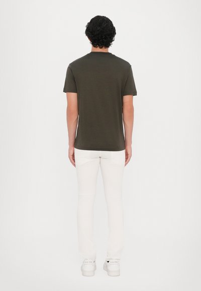 T-shirt vert olive à manches courtes avec un col rond, associé à un jean blanc slim et des baskets blanches, vu de dos.