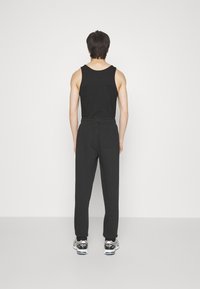 Zwarte tanktop gecombineerd met zwarte broeken met een elastische tailleband, een gladde textuur en een achterzak, gedragen met sneakers.