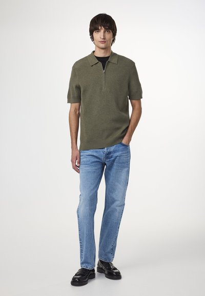 Oliwkowa dzianinowa koszulka polo z zamkiem na szyi, krótki rękaw, w połączeniu z jasnoniebieskimi dżinsami i czarnymi butami wizytowymi. Prosty design, bez wzorów.