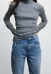 Top à col roulé côtelé gris associé à un jean taille haute déchiré bleu clair. Le tissu semble doux avec une silhouette ajustée.