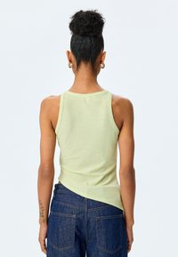 Lys grøn ribbet tanktop med rund halsudskæring, tætsiddende design og asymmetrisk kant; parret med mørkeblå denim jeans.