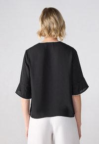 Svart kortermet bluse med utsvingte mansjetter, med rund halslinning og kontrastkant i hvitt. Glatt, lett stoff.
