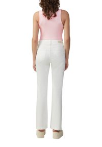 Witte flared jeans met achterzakken, gecombineerd met een roze ribgebreide tanktop. De outfit wordt compleet gemaakt met beige platform schoenen.