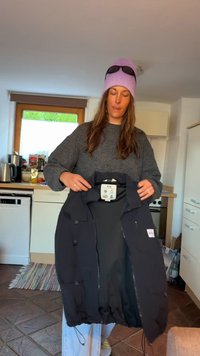 Zwarte jas van waterafstotend materiaal, met een ritssluiting, verstelbare trekkoord onderkant en meerdere zakken. Tags zichtbaar.