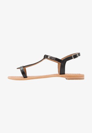 Black leather strappy sandals with a flat wooden sole, featuring a T-bar design and adjustable ankle strap with metal buckle.