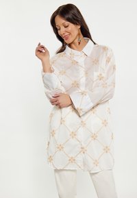 Witte shirt met een opzetkraag, voorzien van een diamanten patroon in lichtbeige borduurwerk. Lange mouwen en een relaxte pasvorm.