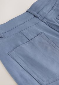 Gros plan sur un tissu bleu clair montrant la poche arrière et les passants de ceinture avec des coutures détaillées sur un pantalon.