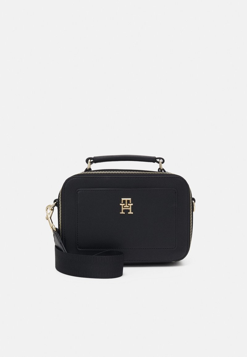Black rectangular crossbody bag made of smooth material, featuring gold hardware, front logo, and adjustable strap. Zipper closure on top.