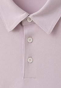 Gros plan d’un col de polo texturé rose pâle avec trois boutons blancs fermés le long de la patte de boutonnage.