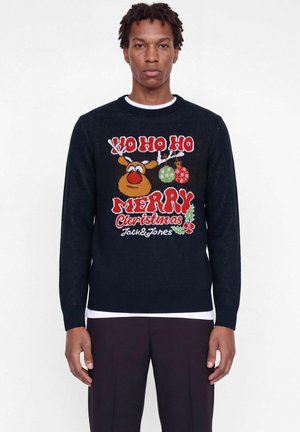 Homme portant un pull de Noël noir avec des rennes, des ornements et un texte rouge affichant "Ho Ho Ho Merry Christmas Jack & Jones."