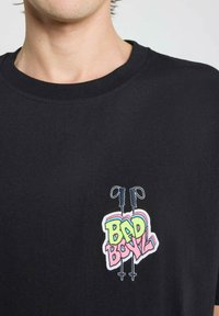 T-shirt en coton noir avec un motif brodé multicolore "BAD BOY" et deux cannes croisées. Encolure ronde, manches courtes.