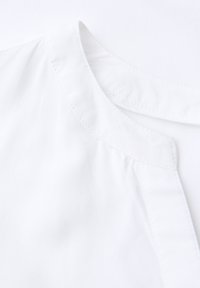 Blusa bianca con scollatura arrotondata, caratterizzata da pieghe leggere e una texture liscia. Il tessuto sembra leggero e fresco.