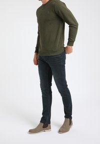 Felpa verde oliva con un motivo testurizzato, abbinata a jeans scuri e stivali alla caviglia in suede grigio con pannelli elastici laterali.