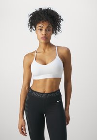 Sujetador deportivo blanco con tirantes finos y banda texturizada con el logotipo "NIKE". Combinado con leggings negros que tienen una cinturilla "NIKE PRO" y acentos verticales.