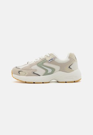 Zapatillas deportivas beige con parte superior de malla y ante, acentos verdes, cordones blancos y suela de goma texturizada. Presenta un logo de la marca en el lateral.