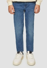 Jasnoniebieskie dżinsy o prostym kroju, z subtelnym wyblaknięciem i klasycznym pięciopocketowym designem. Zestawione z białymi trampkami z granatowymi akcentami.