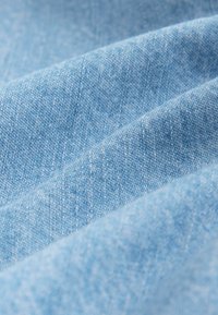Tissu bleu clair présentant une texture lisse avec des motifs de tissage visibles, tombant en plis doux et superposés.