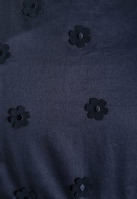 Marinblått tyg med en slät yta, prytt med små svarta tybliljor med runda svarta mittpunkter, jämnt fördelade över ytan.