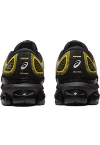 Scarpe da atletica nere e gialle con tomaia in mesh, design curvo, ammortizzazione visibile, logo distintivo e accentuazioni testurizzate.