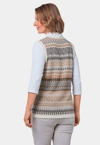 Strickweste mit mehrfarbigen geometrischen Mustern in Braun, Grau und Creme; besteht aus einem weißen Hemdkragen und Dreiviertelärmeln.