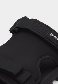 Μαύρο σανδάλι με ρυθμιζόμενους υφασμάτινους ιμάντες και πλαστική αγκράφα, διαθέτει κυρτό πέλμα και ετικέτα με το λογότυπο της μάρκας "CAMPER".