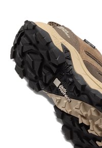 Semelle de chaussure de randonnée avec des crampons profonds noirs et beiges, adhérence texturée, logo Jack Wolfskin et étiquette en tissu Texapore sur la tige marron.