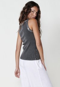 Grijze geribde tanktop met een aansluitend ontwerp, voorzien van decoratieve accenten langs de schoudernaad, gecombineerd met witte wijde broek.