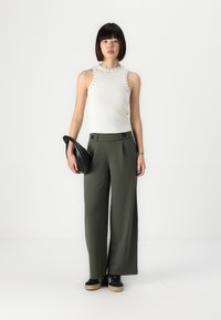 Witte mouwloze top met studs bij de halslijn, gecombineerd met olijfgroene hoge taille wijde broek en een zwart clutch.