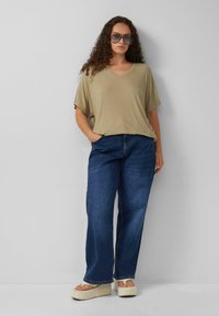 Beige geribbelde V-hals top met brede korte mouwen, gecombineerd met losse blauwe denim jeans en beige platform sandalen. Duidelijke zonnebril is gedragen.