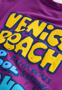 Lila szövet nagy sárga "VENICE BEACH" felirattal, és kisebb kék és fekete szöveg, amelyen az áll: "BREAK BEATS SCRATCHES POOL."
