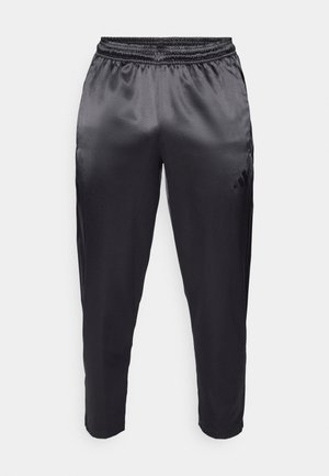 Zwarte sportbroek gemaakt van gladde, lichte stof met een elastische tailleband. Heeft een klein logo aan de linkerkant en taps toelopende pijpen.