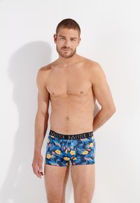 Boxers ajustados para hombre en un patrón floral azul con flores amarillas y hojas verdes. Con una cinturilla elástica negra con logo.