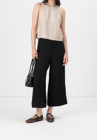 Beiges ärmelloses Oberteil, schwarze weit geschnittene Hose, Leopardenmuster-Ballerinas und eine kleine schwarze Handtasche mit doppelten Griffen. Glatte Texturen, lockere Passform.