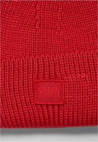 Červená pletená čepice s ribbed texturou, se čtvercovou nášivkou vyraženou s nápisem "URBAN CLASSICS" na přední straně.