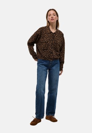 Veste chemise en imprimé léopard marron avec fermeture à boutons, associée à un jean en denim bleu et des mocassins en suède marron. Coupe et texture décontractées.