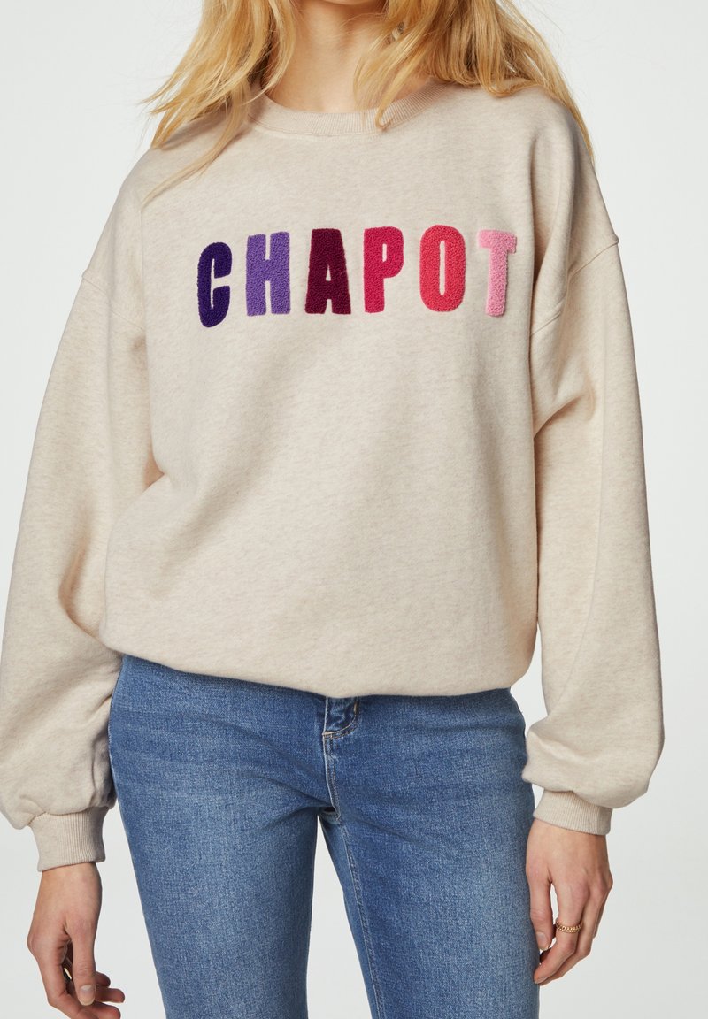 Felpa beige con vestibilità over-size, caratterizzata dalla scritta "CHAPOT" in un ricamo vivace e audace. Maniche lunghe, polsini a coste e un morbido tessuto.