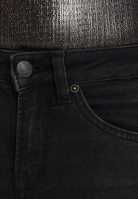 Jeans de mezclilla negra con un diseño clásico de cinco bolsillos, cierre de botón plateado y un ligero desgaste en la textura.