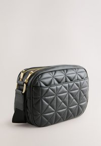 Sort quiltet lædertaske med guldlynlåse og beslag, med en rektangulær form og justerbar rem.