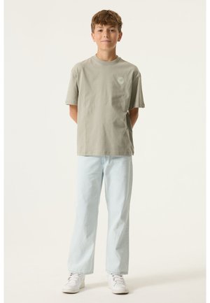 Lichtgrijs katoenen T-shirt met korte mouwen en een kleine spiraalafbeelding op de borst, gecombineerd met lichtblauwe jeans met rechte pijpen en witte sneakers.