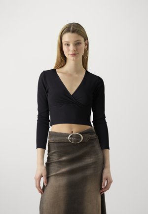 Crna rebrasta dug sleeves crop majica s dubokim V-izrezom, u kombinaciji s smešnom suknjom visokog struka koja ima veliki srebrni kopč.