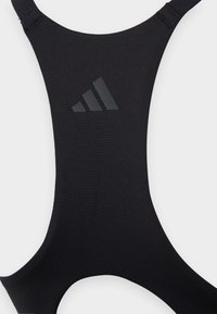 Svart sportsbh laget av mykt, elastisk stoff. Har brede stropper og en hevet svart logo på fronten. Enkelt, minimalistisk design.