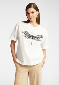 T-shirt in cotone bianco con una stampa grafica di una libellula nera. Maniche corte, colletto rotondo, vestibilità comoda e texture liscia.