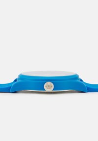 Modré silikónové hodinky s okrúhlym ciferníkom, priehľadným sklom a strieborným logom. Majú hladký povrch a žiadne viditeľné vzory.