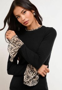 Crna majica sa leopard uzorkom na rubovima rukava i vratnom izrezu. Mekana tekstura, prilagođeni dizajn, s delikatnim rubom na ruffles.