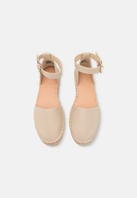 Beżowe skórzane sandały espadryle z paskiem na kostkę, plecioną juty podeszwą i gładką teksturą. Otwarty tył i okrągły nos.