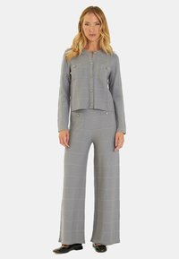 Completo grigio a due pezzi con texture, composto da un giubbino corto con bottoni e pantaloni a gamba larga con motivi orizzontali. Accentuato da bottoni metallici.