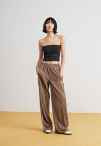 Black lace strapless top and brown track pants with white side stripes and Adidas logo, paired with white sneakers on a yellow floor.