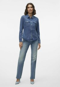 Jeanshemd in Mittelblau, tailliert mit zwei Brusttaschen, kombiniert mit hellblauen, geraden Jeans und hellblauen High Heels.
