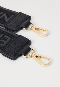 Black leather strap with textured surface and gold-tone metal clasps, featuring branding detail on the hardware.